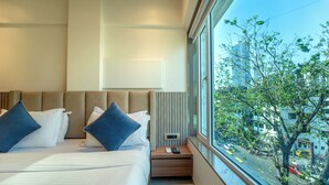 A hotel room with a large bed, a nightstand, a remote control, and a view of the city through a large window. - Hotel Kalpana Palace (Mumbai)