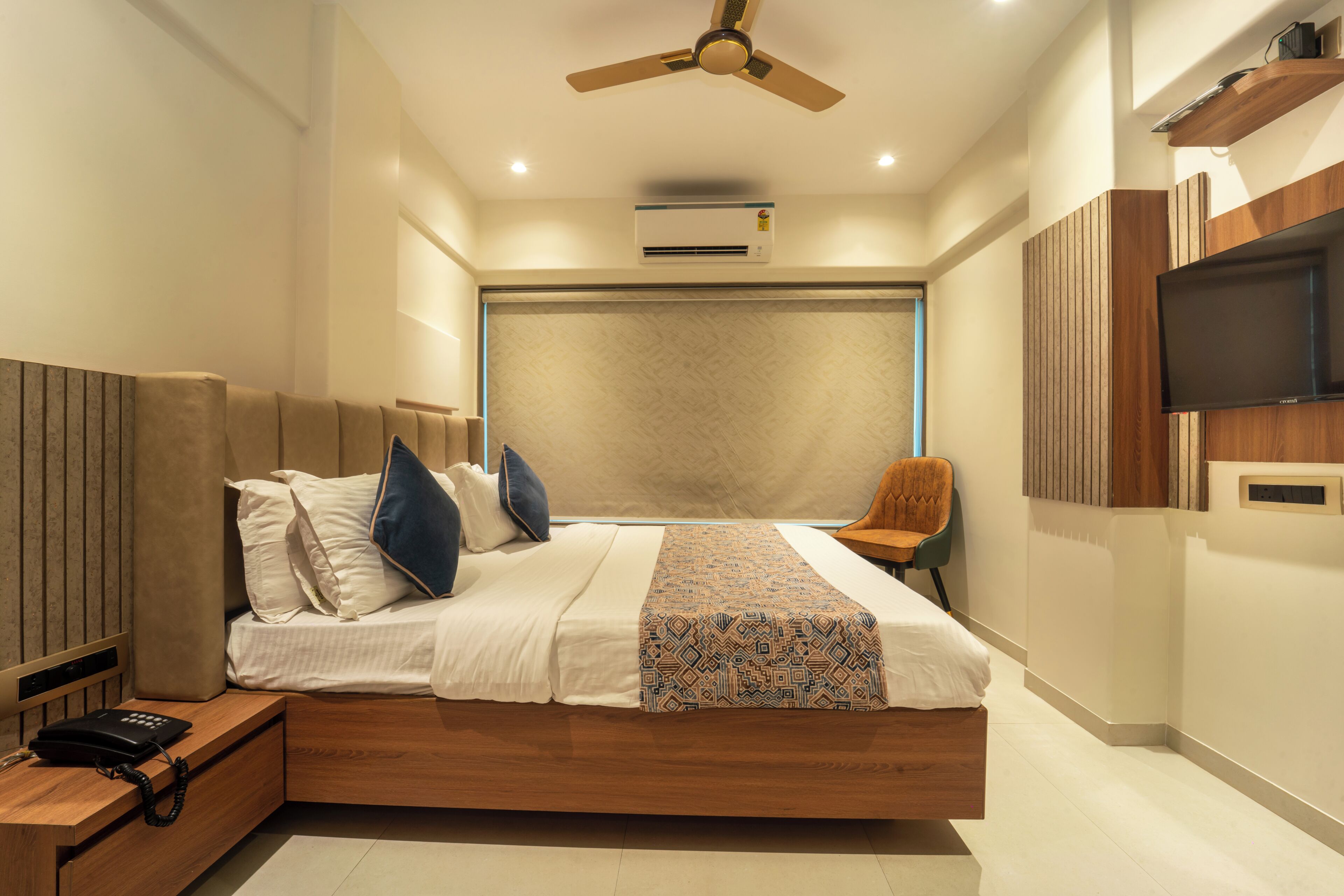 A modern bedroom with a bed, bedside table, chair, TV, and ceiling fan.