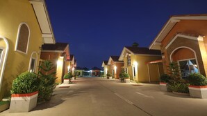 A residential street at dusk with houses featuring arched doorways and a central driveway. - Windsor Park and Resort (Lop Buri)