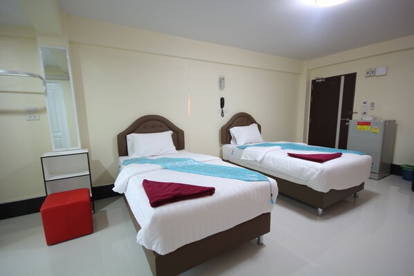 A hotel room with two beds, a red stool, a wardrobe, and a desk.