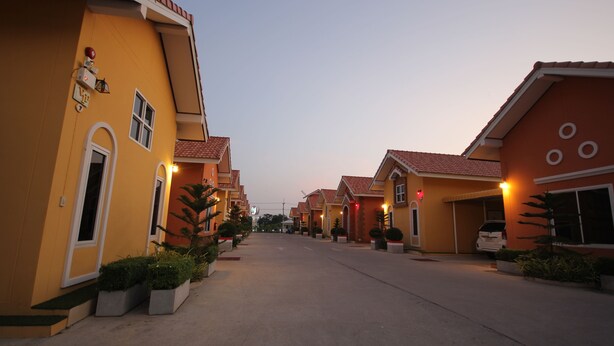 A residential street with yellow houses, each with a garage and potted plants. - Windsor Park and Resort (Lop Buri)