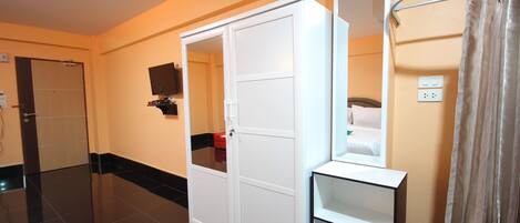 A hotel room with a white wardrobe, a purple bench, a mirror, and a shower area.