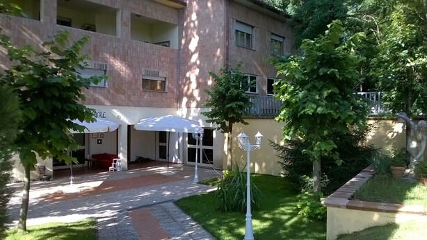 A courtyard with a red sofa, white umbrellas, and a statue. - Villa Cardinal Apartments (Tivoli)