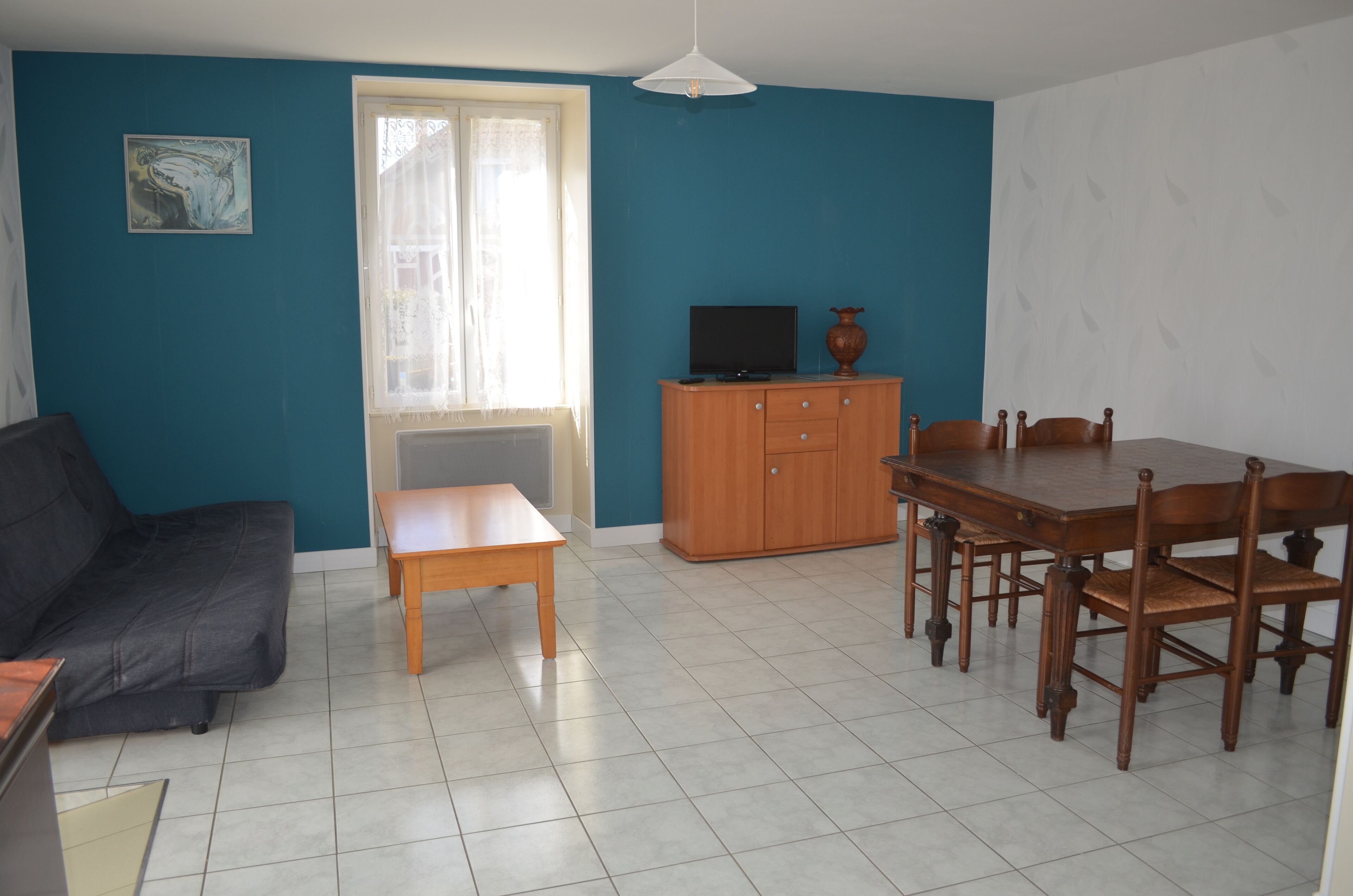 Ein Wohnzimmer mit einer Couch, einem kleinen Tisch, einem Fernseher auf einer Holzkommode und einem Esstisch mit Stühlen.