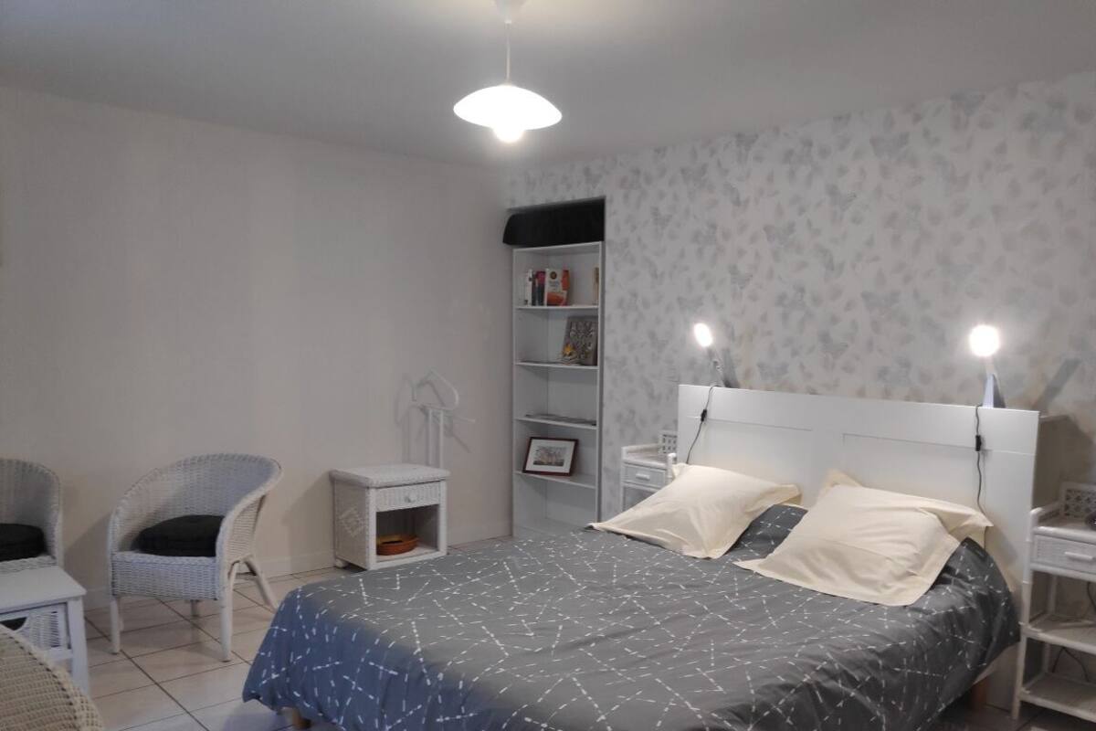 A bedroom with a bed, two bedside tables, a chair, a nightstand, and a shelf unit.