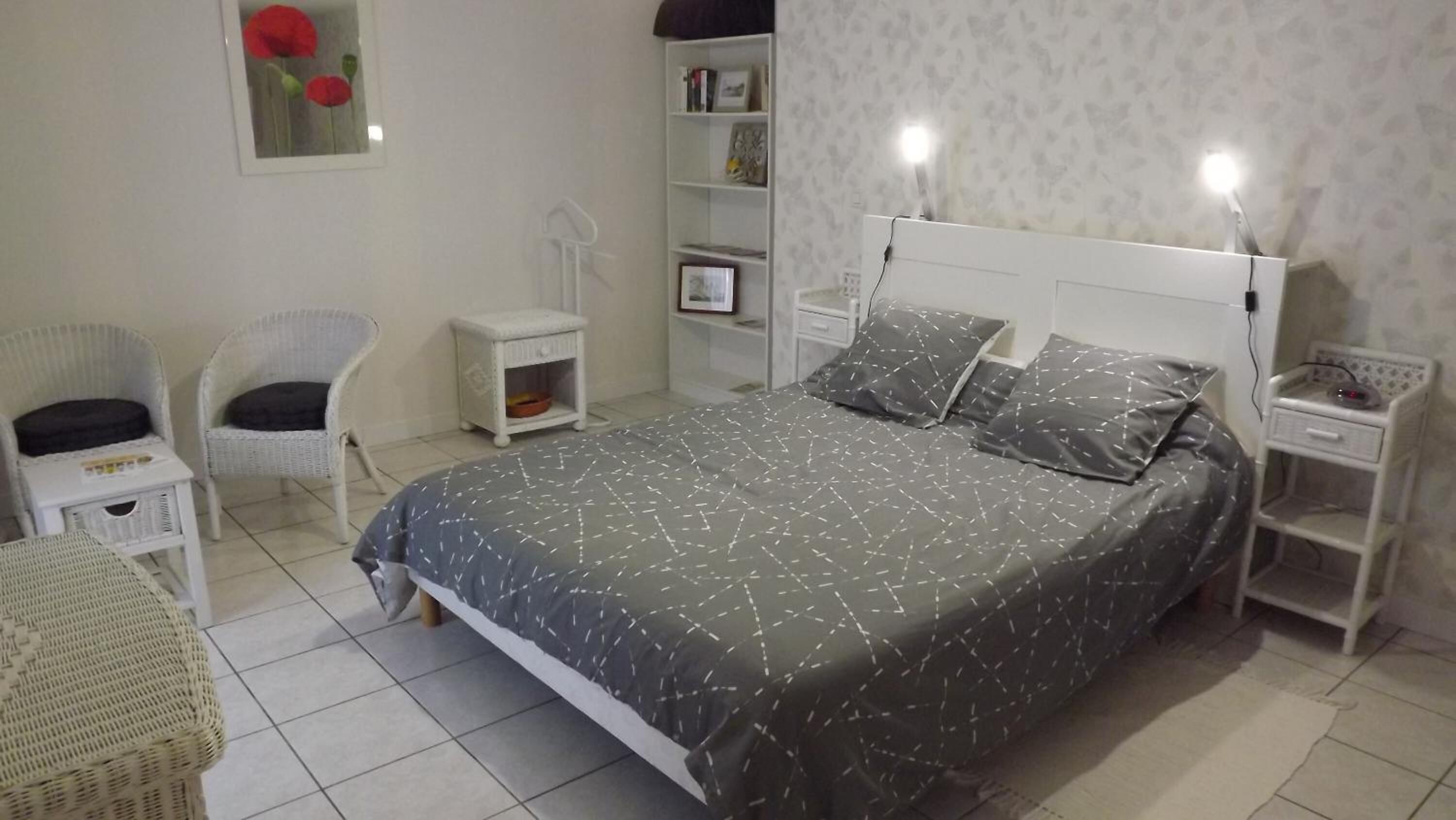 A neatly arranged bedroom with a bed, two chairs, a small table, and a bedside table with lamps.
