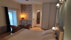 A hotel room with a large bed, a desk with a chair, a bookshelf, and a door leading to another room. - Logis De Chezelles (Sidiailles)