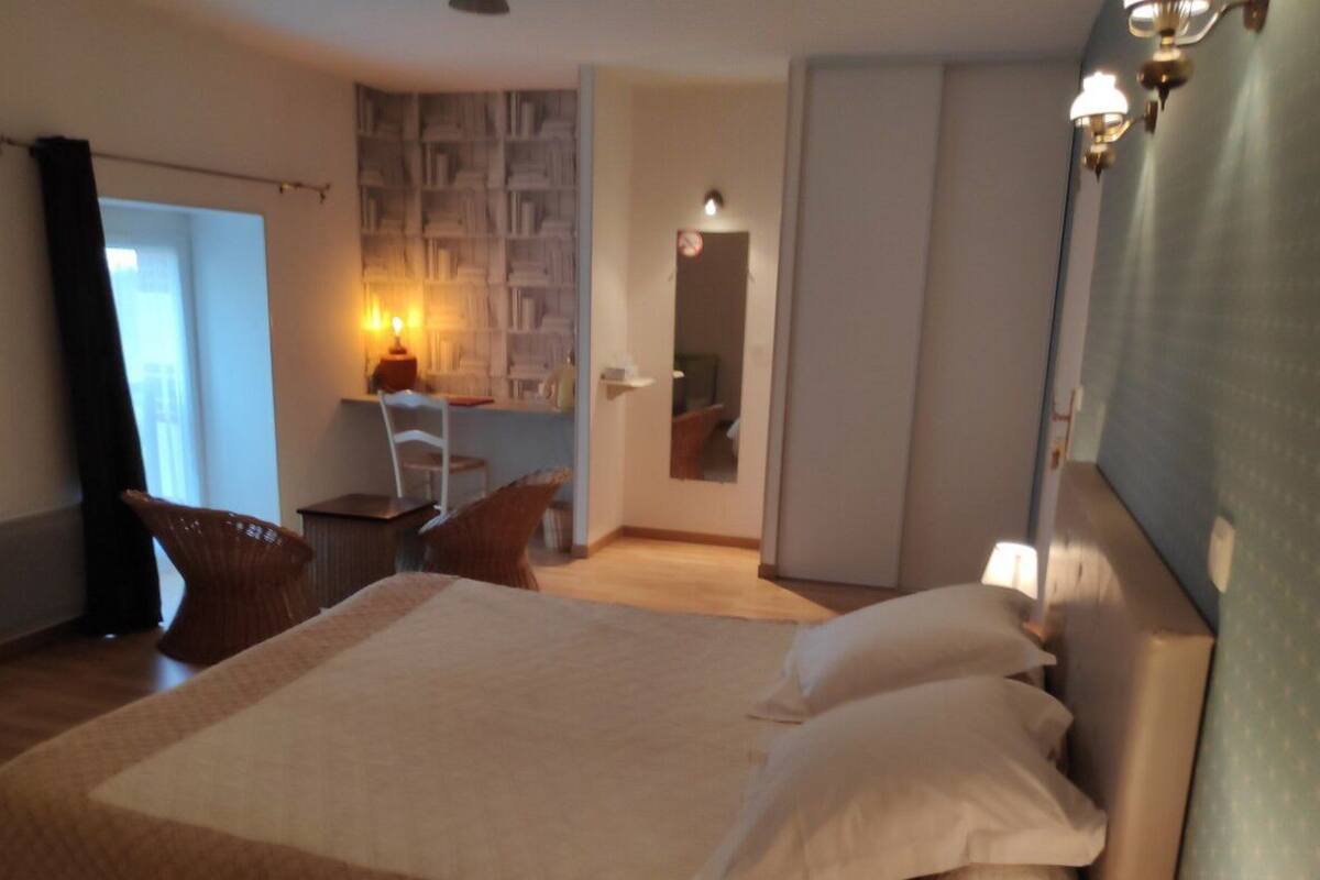A hotel room with a large bed, a desk with a chair, a bookshelf, and a door leading to another room.
