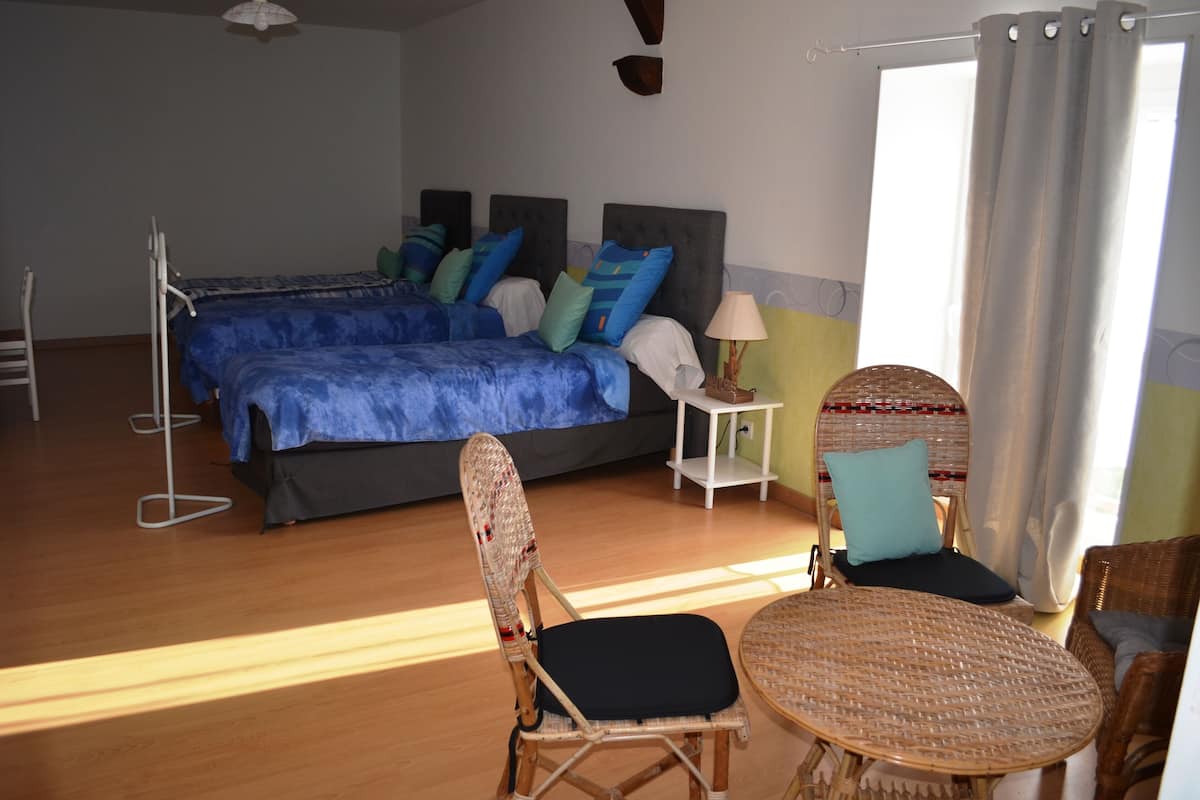 A bedroom with a bed, two chairs, a small table, and a window with curtains.