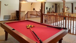 A pool table with a red felt surface, two pool cues, and a cue ball in a room with wooden railings and a staircase. - Logis De Chezelles (Sidiailles)