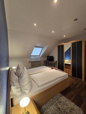 Une chambre à coucher comprenant un lit, un bureau, une chaise, une armoire et une fenêtre de toit.