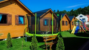 A row of wooden cabins with a trampoline in the center, surrounded by small trees and a playground. - Nemo Domki Letniskowe (gmina Wolin)