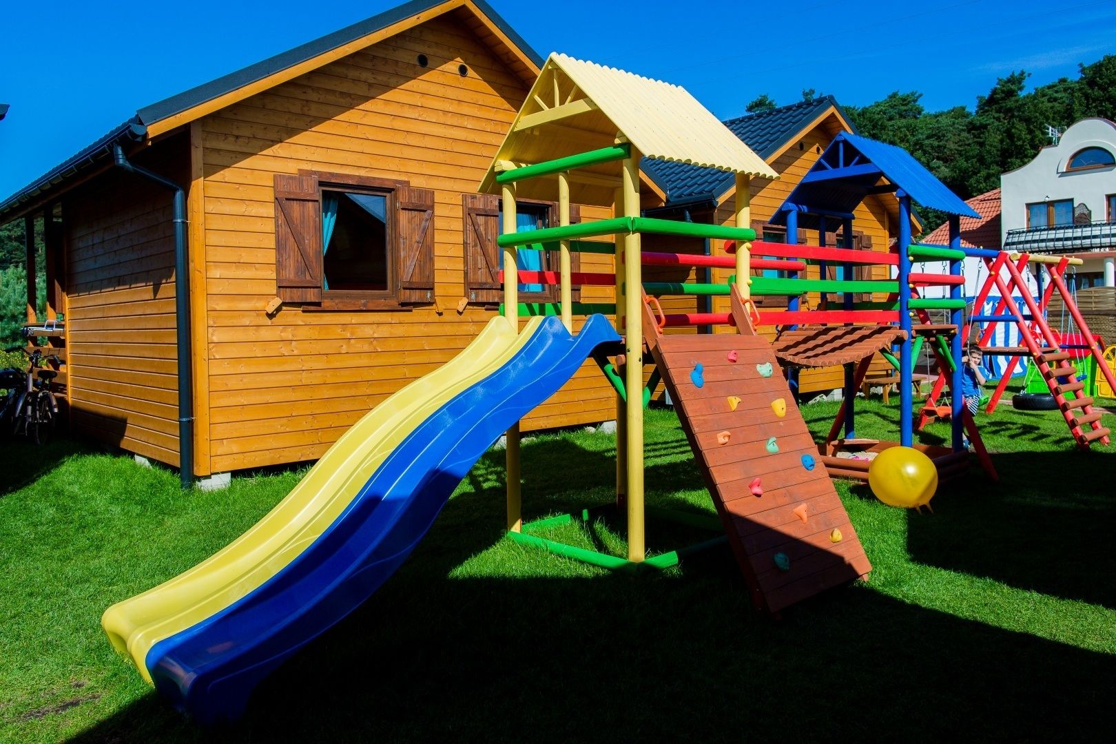 A wooden play structure with a slide and climbing wall, adjacent to a small wooden building.