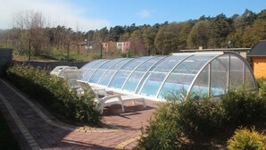 A greenhouse structure with a semi-transparent roof, surrounded by a brick pathway and greenery. - Nemo Domki Letniskowe (gmina Wolin)