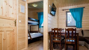 A wooden cabin with bunk beds, a dining table with chairs, and a TV mounted on the wall. - Nemo Domki Letniskowe (gmina Wolin)