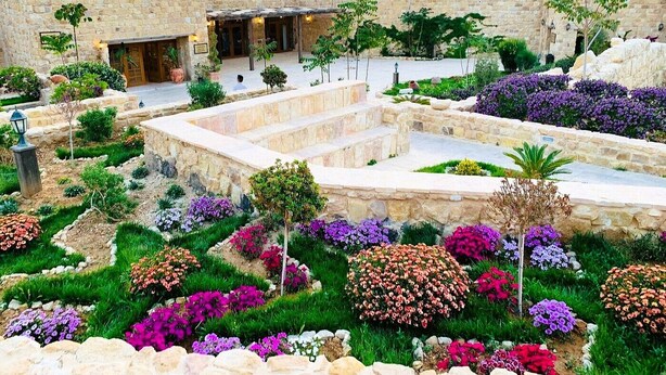 A courtyard with stone walls, a covered seating area, and a variety of colorful flowers. - Old Village Resort (Wadi Musa)