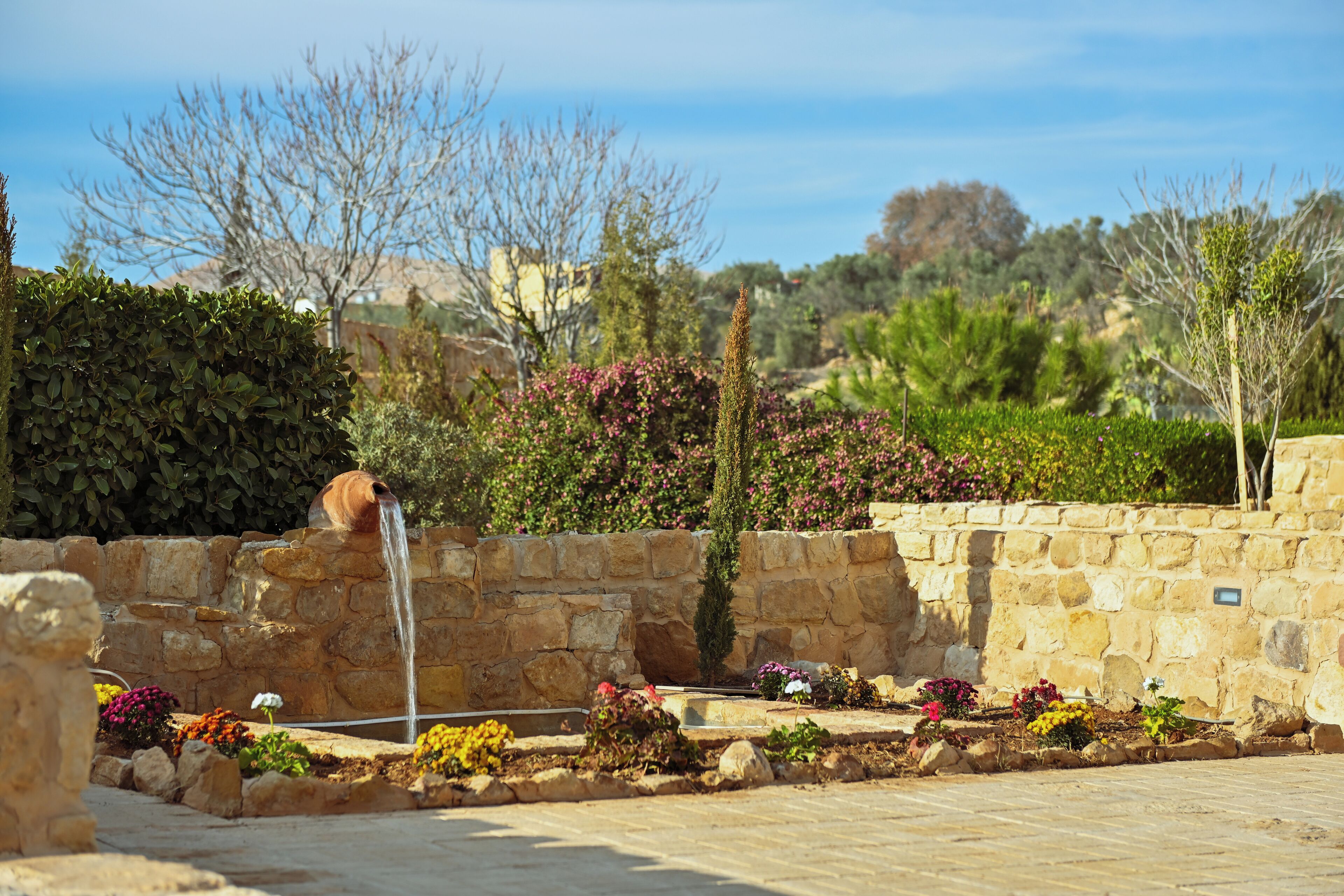 Muro de piedra con una fuente de agua y un jardín con diversas plantas y flores.