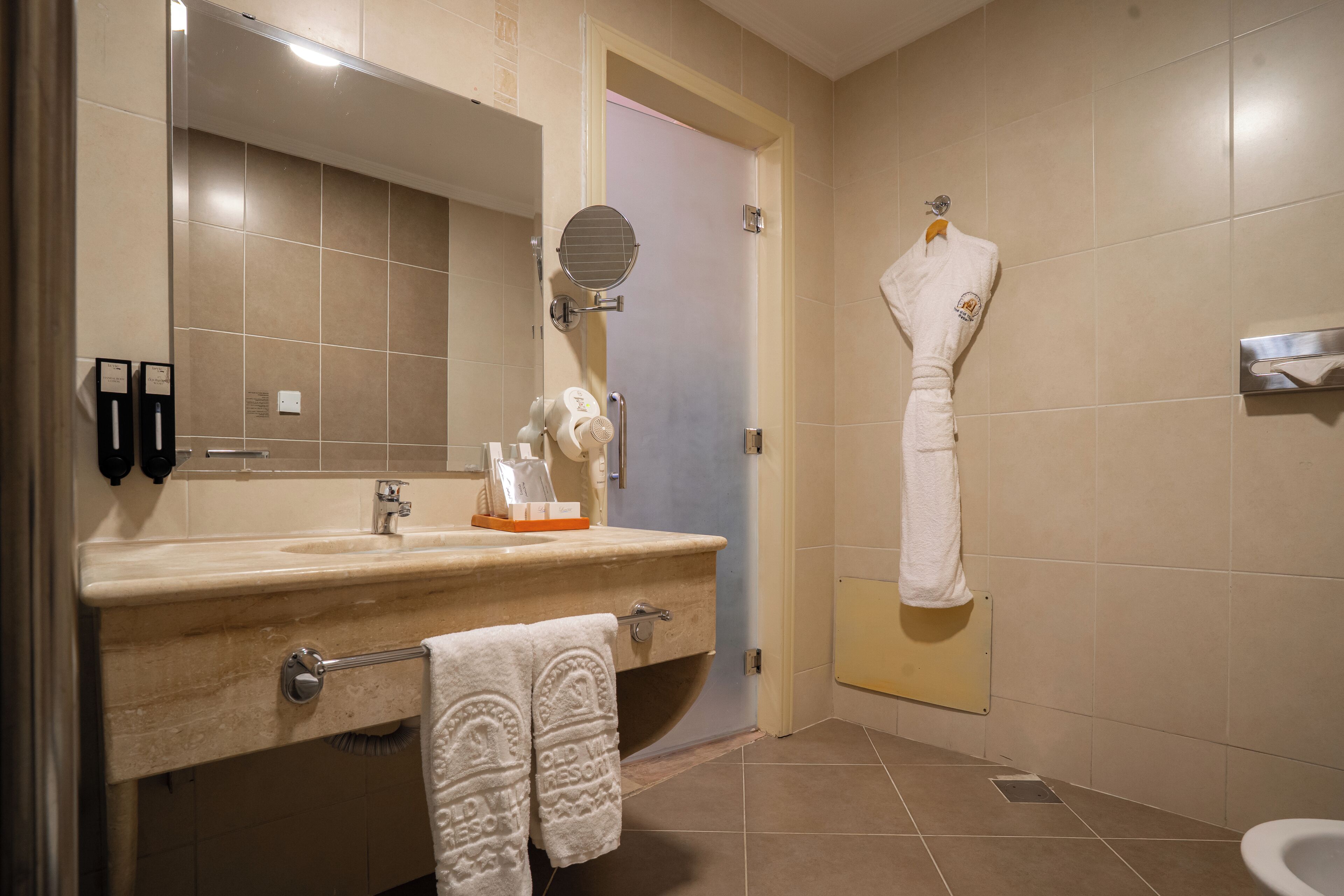Une salle de bain équipée d’un lavabo, d’un miroir, d’un porte-serviettes et d’une serviette accrochée au mur.