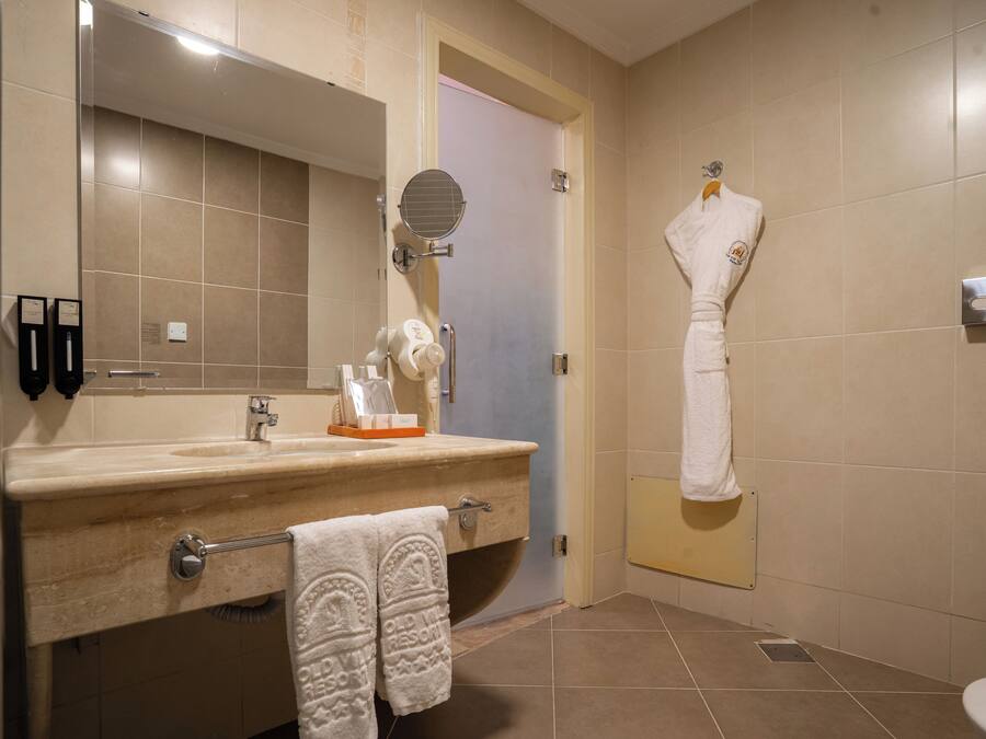 Une salle de bain équipée d’un lavabo, d’un miroir, d’un porte-serviettes et d’une serviette accrochée au mur.