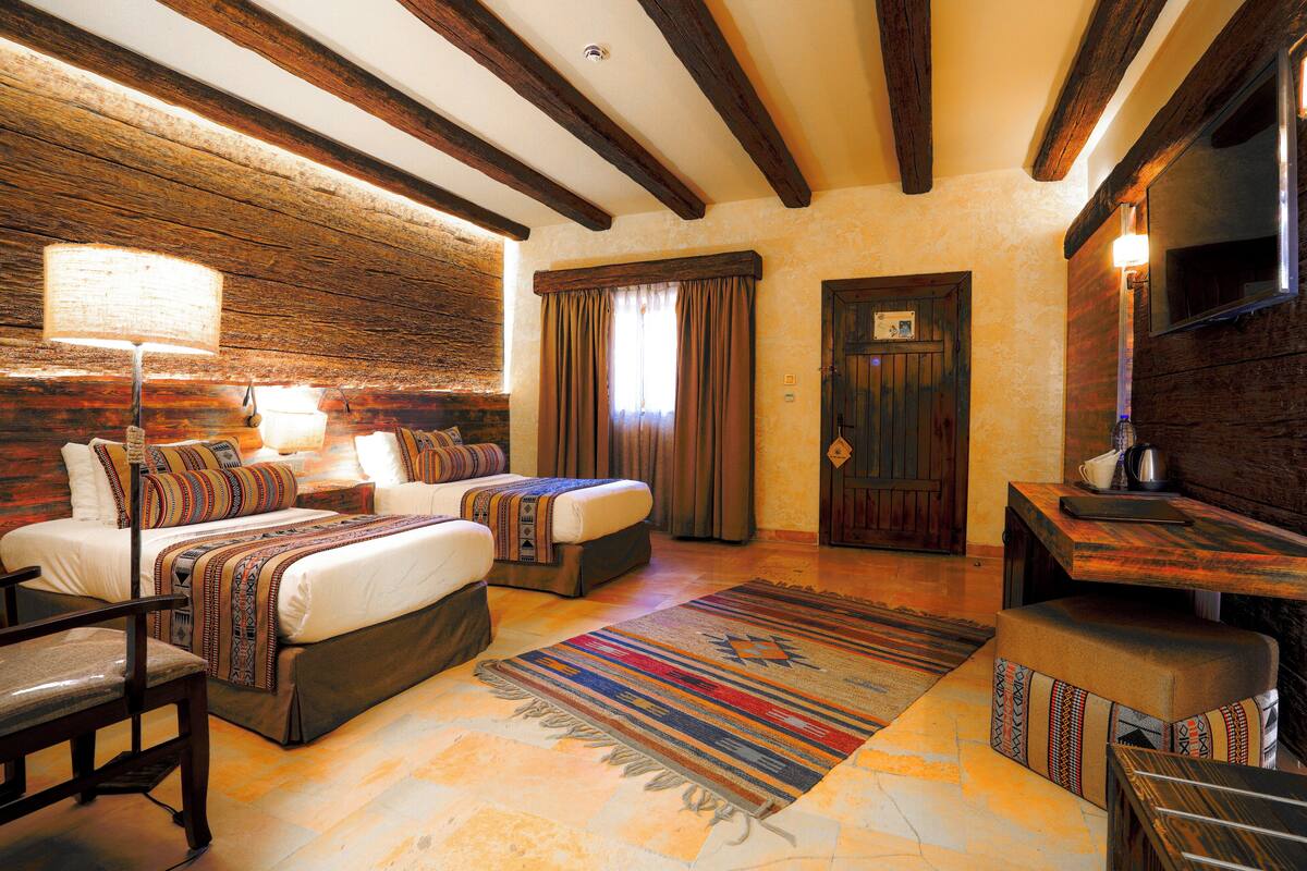 A cozy bedroom with two beds, a sitting area with a table, and a large window with curtains.