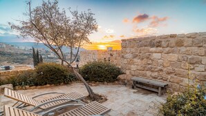 A stone wall with a bench and lounge chairs in a courtyard. - Old Village Resort (Wadi Musa)