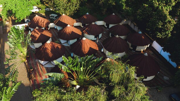 A series of dome-shaped structures with white walls and brown roofs, arranged in a semi-circular pattern, surrounded by lush greenery. - Keys Hotel (Moshi)