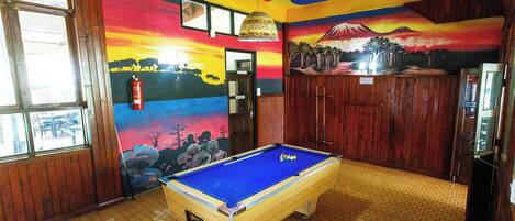 Una mesa de billar en una habitación con paredes de madera y un mural que representa un atardecer y un paisaje montañoso.