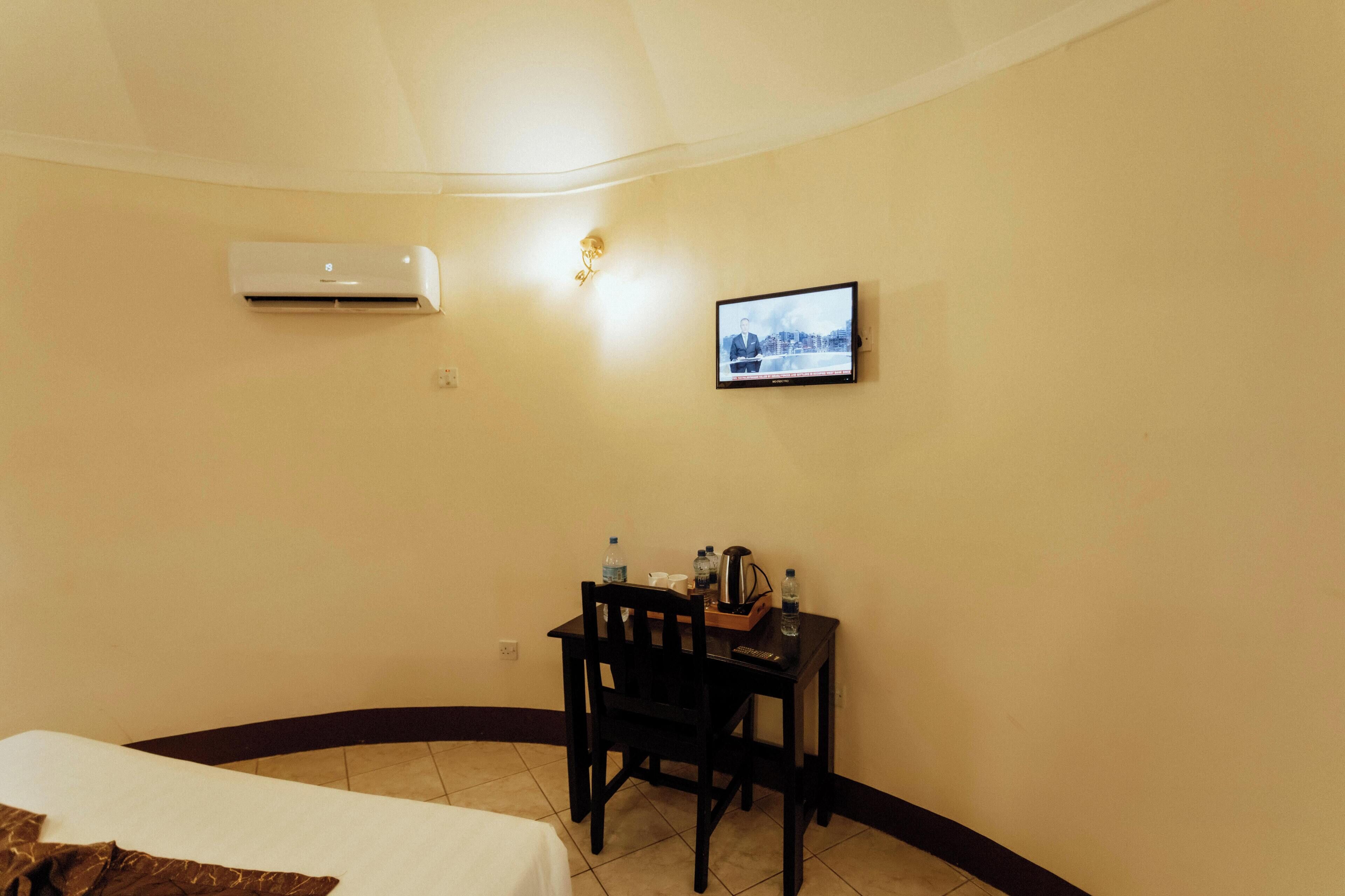 A hotel room with a bed, a desk with a chair, a television, and an air conditioning unit.