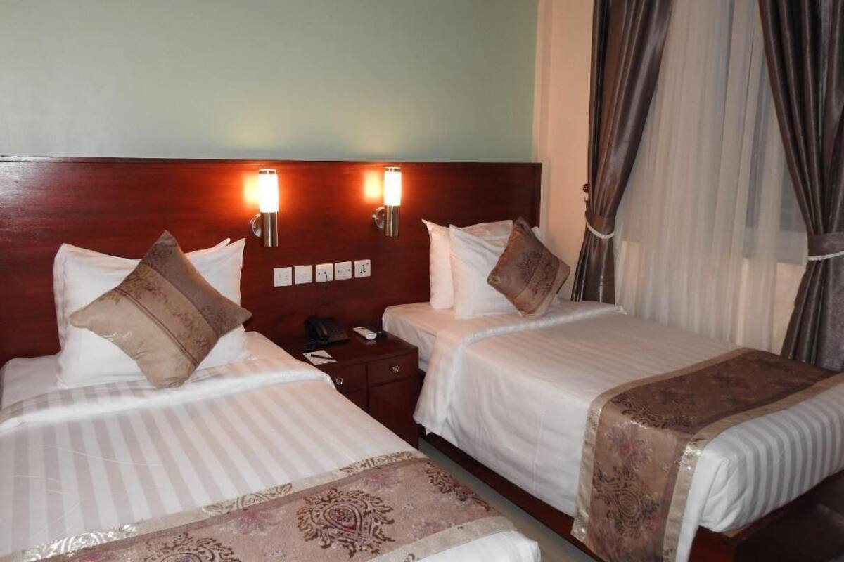 Una habitación de hotel con dos camas, lámparas de noche, una mesita de noche y una ventana con cortinas.