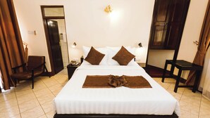A neatly made bed with white linens and two brown pillows, a bedside table with a lamp, and a chair in a hotel room. - Keys Hotel (Moshi)