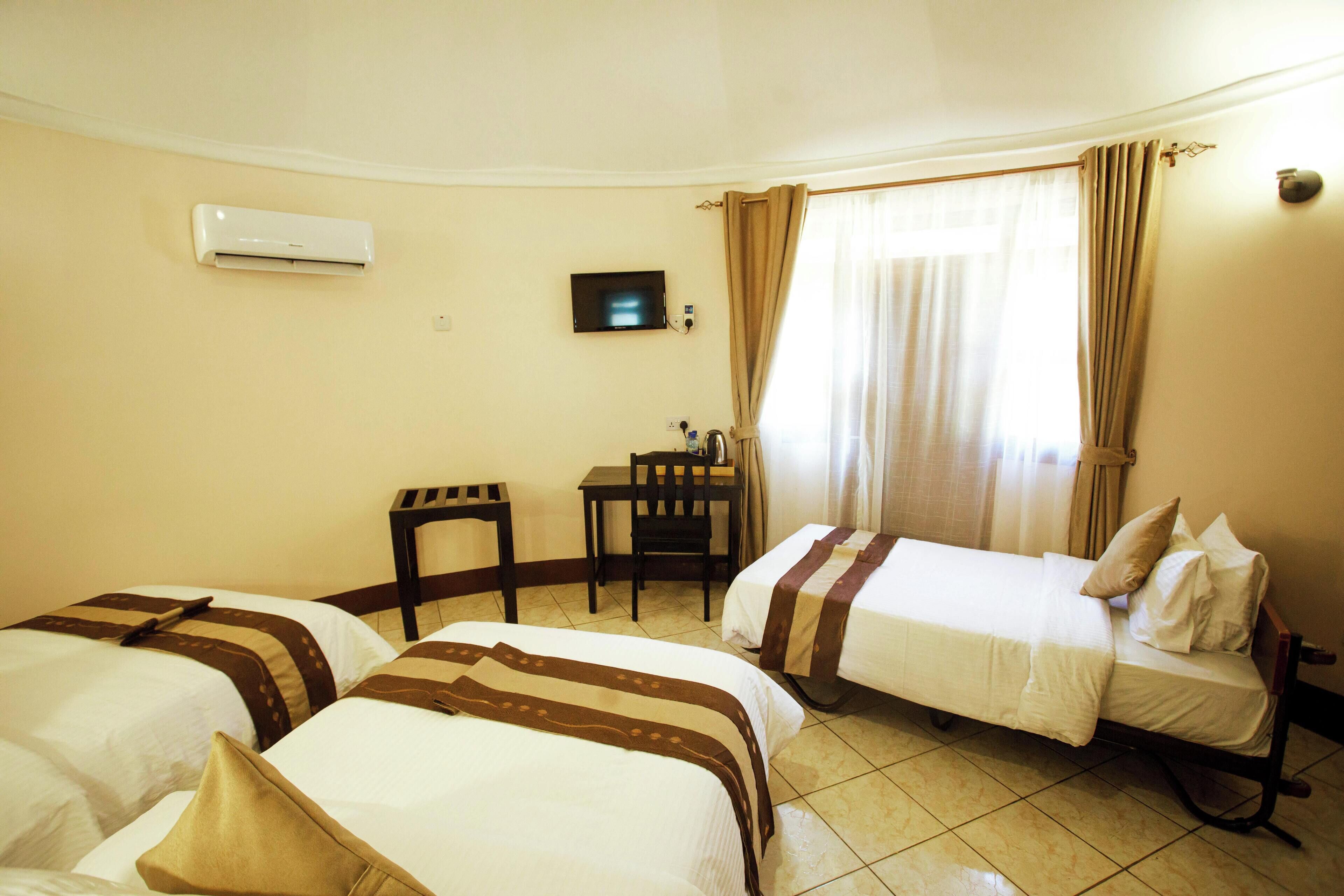 A hotel room with two beds, a desk, a chair, an air conditioning unit, and a television.