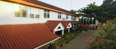 A building with a red-tiled roof and white walls, featuring multiple windows and air conditioning units.