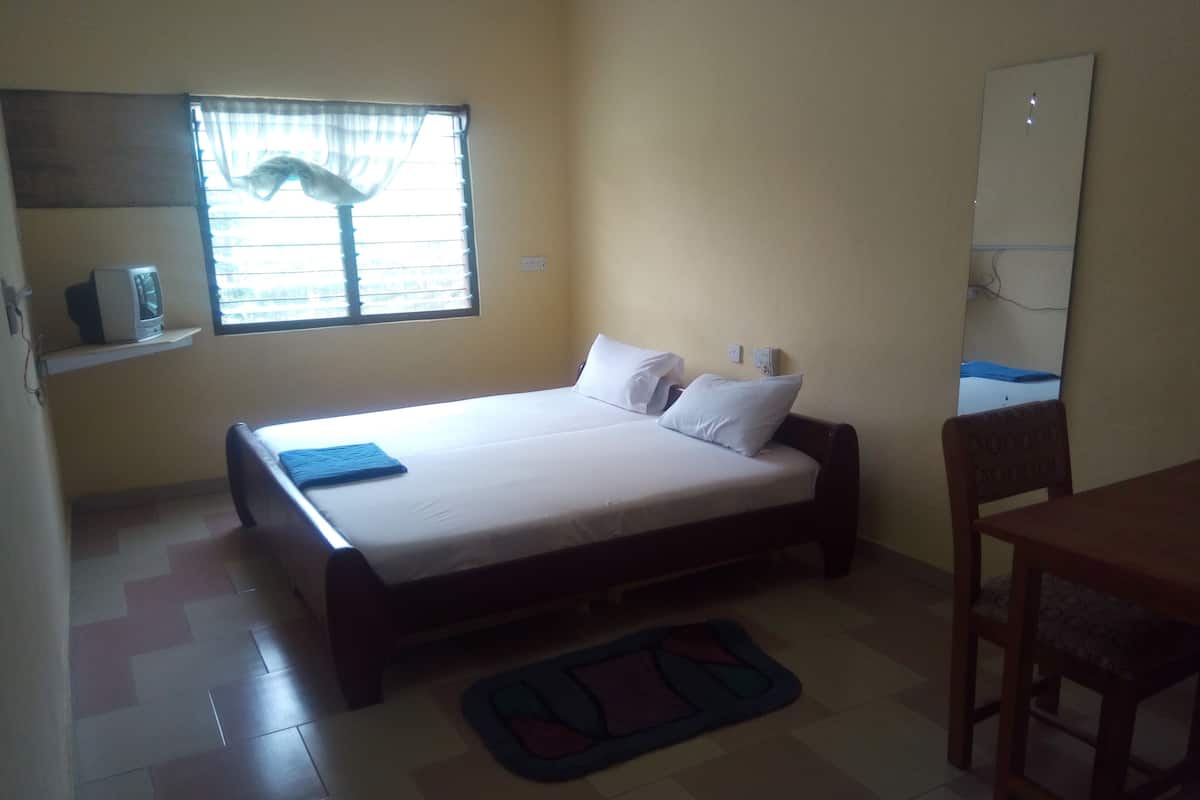 A single-bed room with a window, a bedside table, a chair, and a small rug.