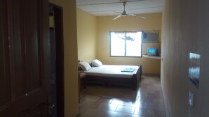 A hotel room with a bed, a ceiling fan, a window with curtains, and an air conditioning unit.