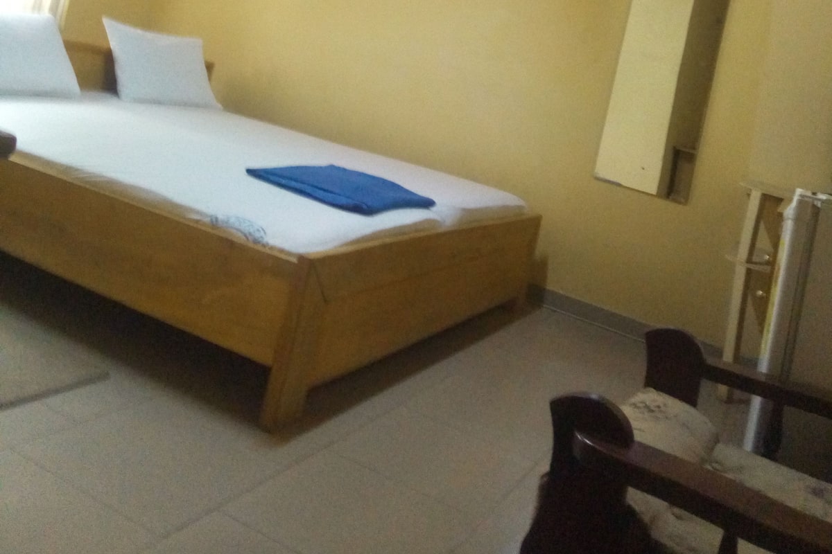 A bedroom with a bed, a ceiling fan, an air conditioning unit, and a mirror on the wall.
