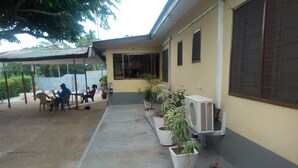 A building with a covered outdoor seating area, potted plants, and an air conditioning unit.