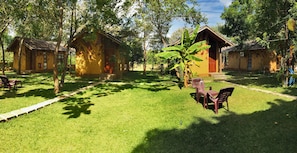 A courtyard with several wooden huts, a grassy lawn, and a few plastic chairs.