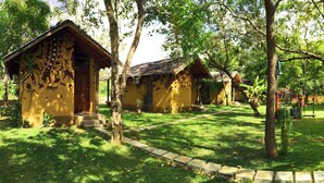 A row of yellow cabins with thatched roofs, surrounded by trees and a well-maintained lawn. - Sat Nam Village Hotel (Avudangawa)