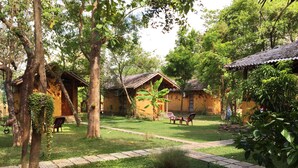 A courtyard with wooden buildings, a paved walkway, and outdoor seating. - Sat Nam Village Hotel (Avudangawa)