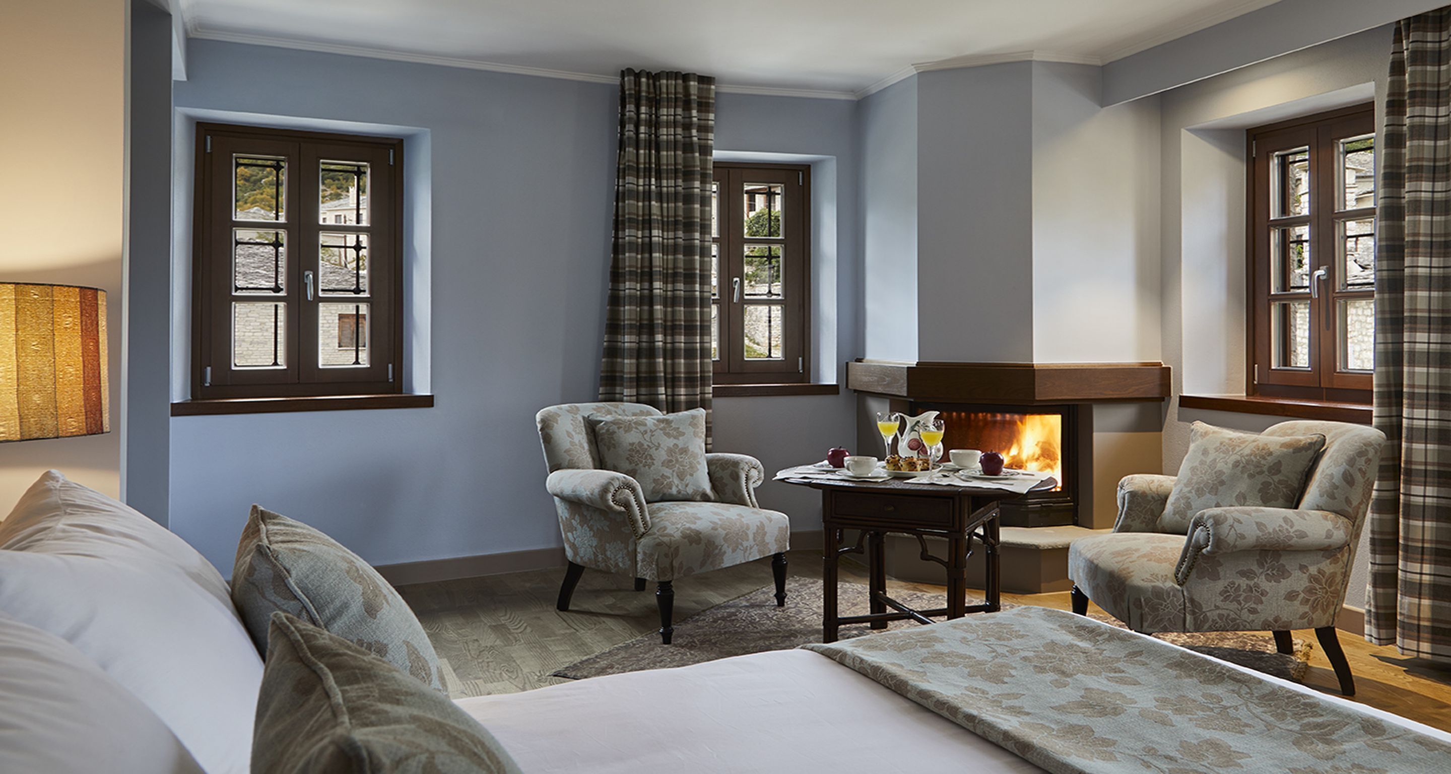 A hotel room with a fireplace, two armchairs, a sofa, and a table with a tea set.