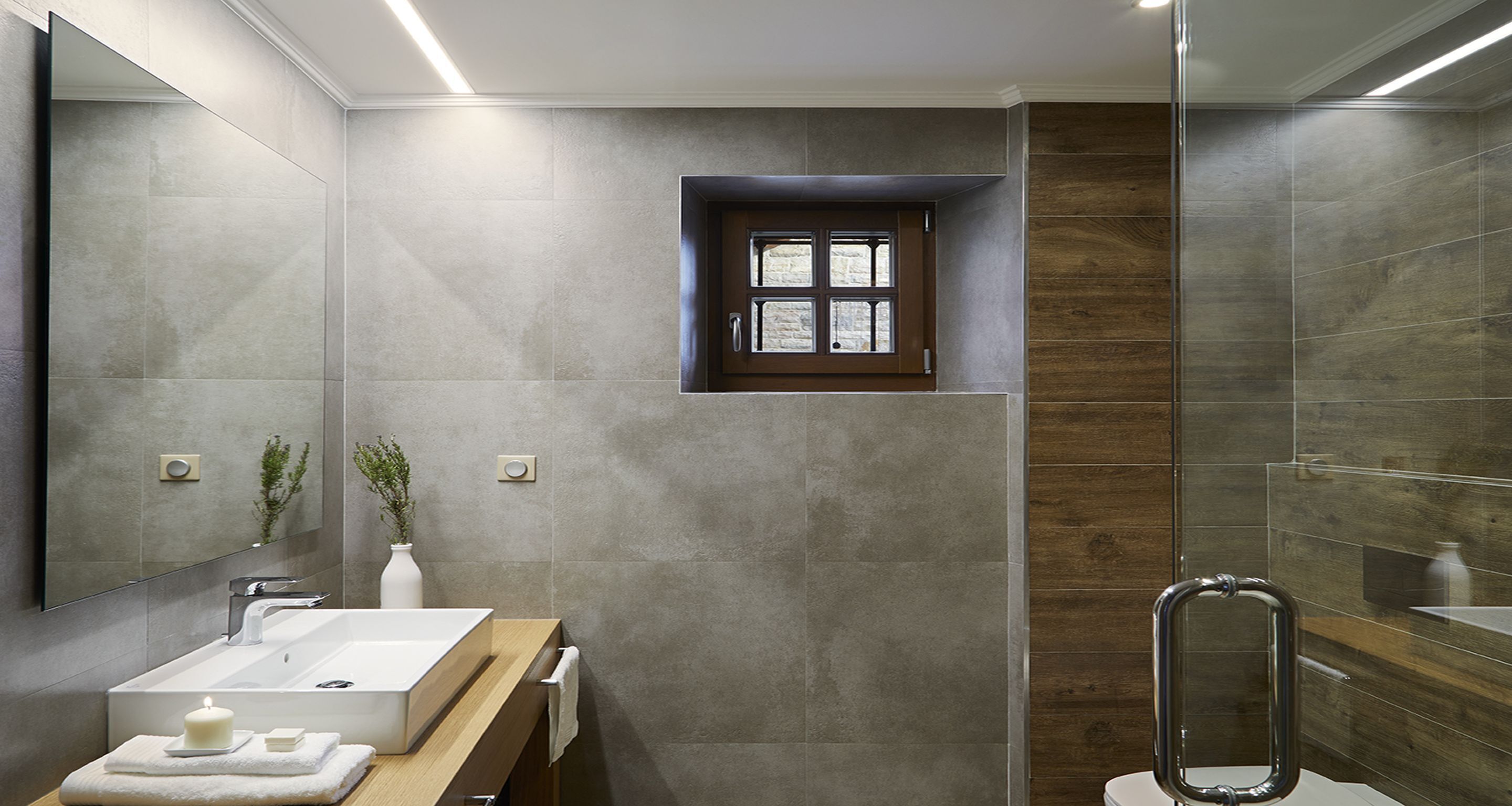 Une salle de bain moderne avec un grand miroir, un lavabo rectangulaire, une fenêtre et une douche en verre.