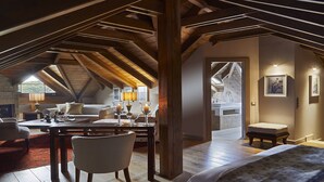 An attic bedroom with a sloped ceiling, a fireplace, a dining area with a table and chairs, and a view of the bathroom. - MounTrace Suites & Spa (Zagori)