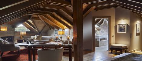An attic bedroom with a sloped ceiling, a fireplace, a dining area with a table and chairs, and a view of the bathroom.