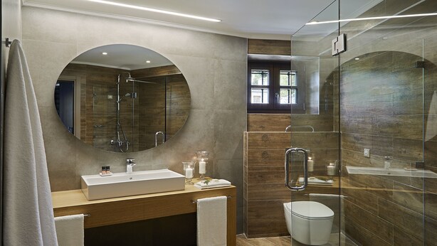 A modern bathroom with a large mirror, a sink, a toilet, and a shower area. - MounTrace Suites & Spa (Zagori)