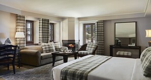 A hotel room with a bed, a sofa, a chair, a small table, and a fireplace. - MounTrace Suites & Spa (Zagori)