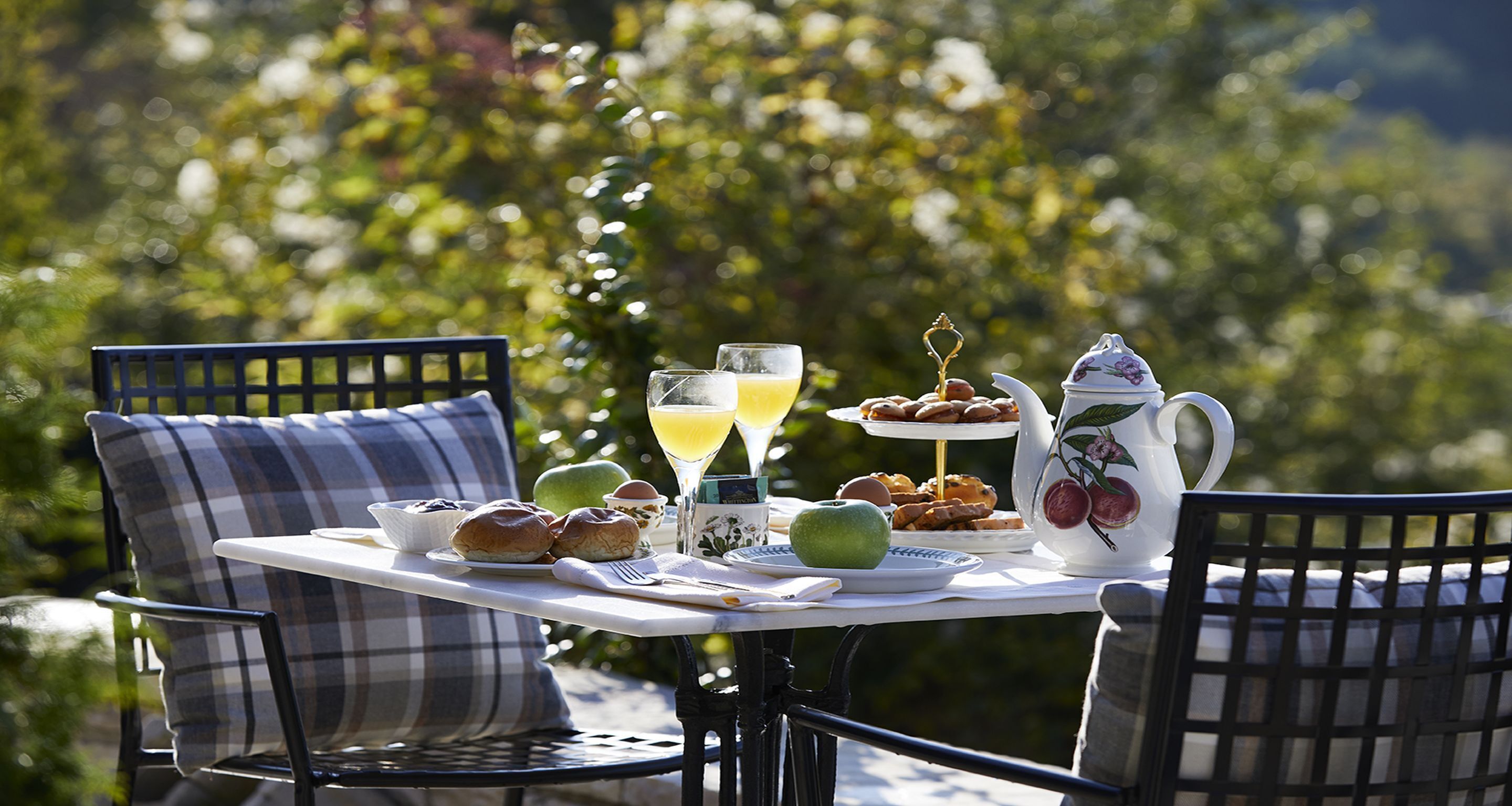 An outdoor dining table with breakfast items, a pitcher, and a glass of orange juice.