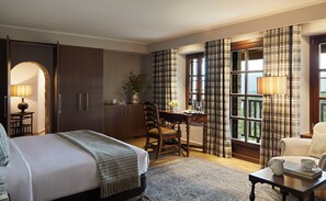 A hotel room with a bed, a desk, a chair, a dining table, and a view through the window. - MounTrace Suites & Spa (Zagori)