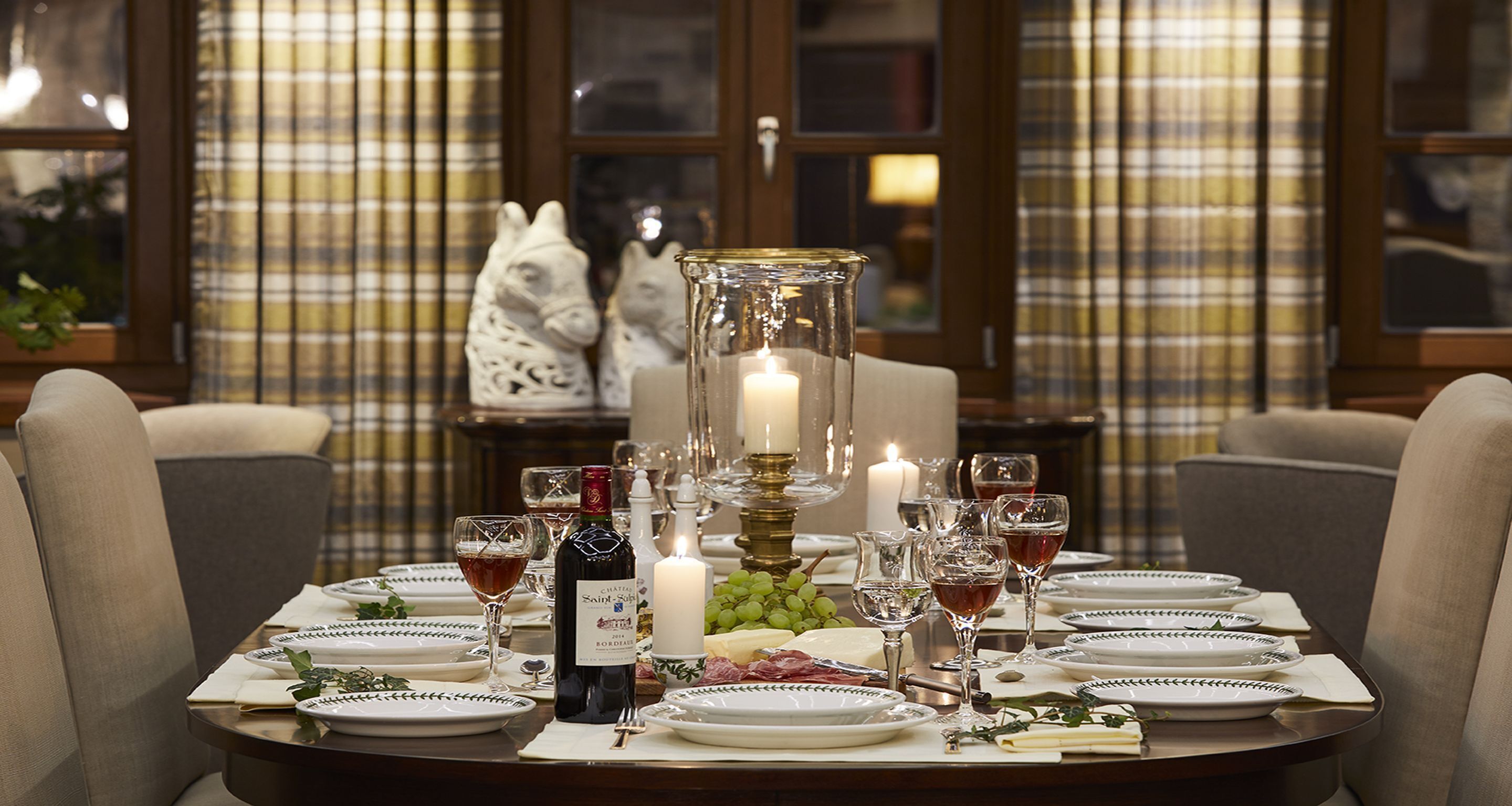 A dining table set for a meal with plates, glasses, a bottle of wine, and a candle.