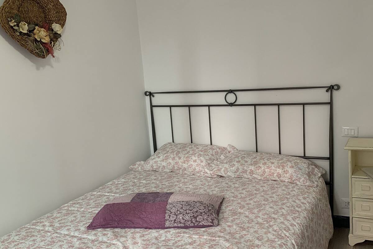 A bed with a floral bedspread, a purple throw pillow, and a decorative basket on the wall.