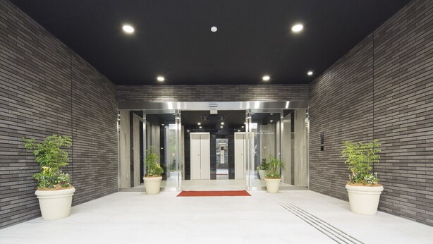 A modern hotel entrance with a brick wall, two potted plants, and an elevator. - SHIZUTETSU HOTEL PREZIO Hakata-Ekimae (Fukuoka)